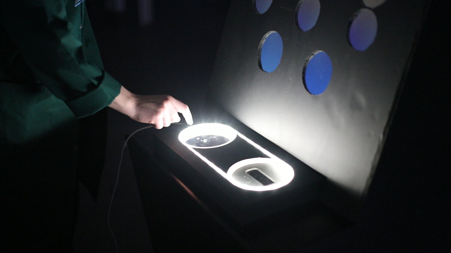 One of the mission consoles in action: a visitor presses a capacitive pad next to projected circular icons, activating the next animated scenario slice in the loop of 2050, 2080, and 2100 missions.